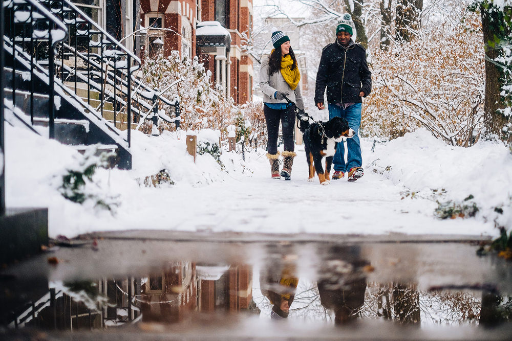 Emmy and James strolling through their snowy neighborhood with their Bernese Mountain Dog Otis during their engagement session.