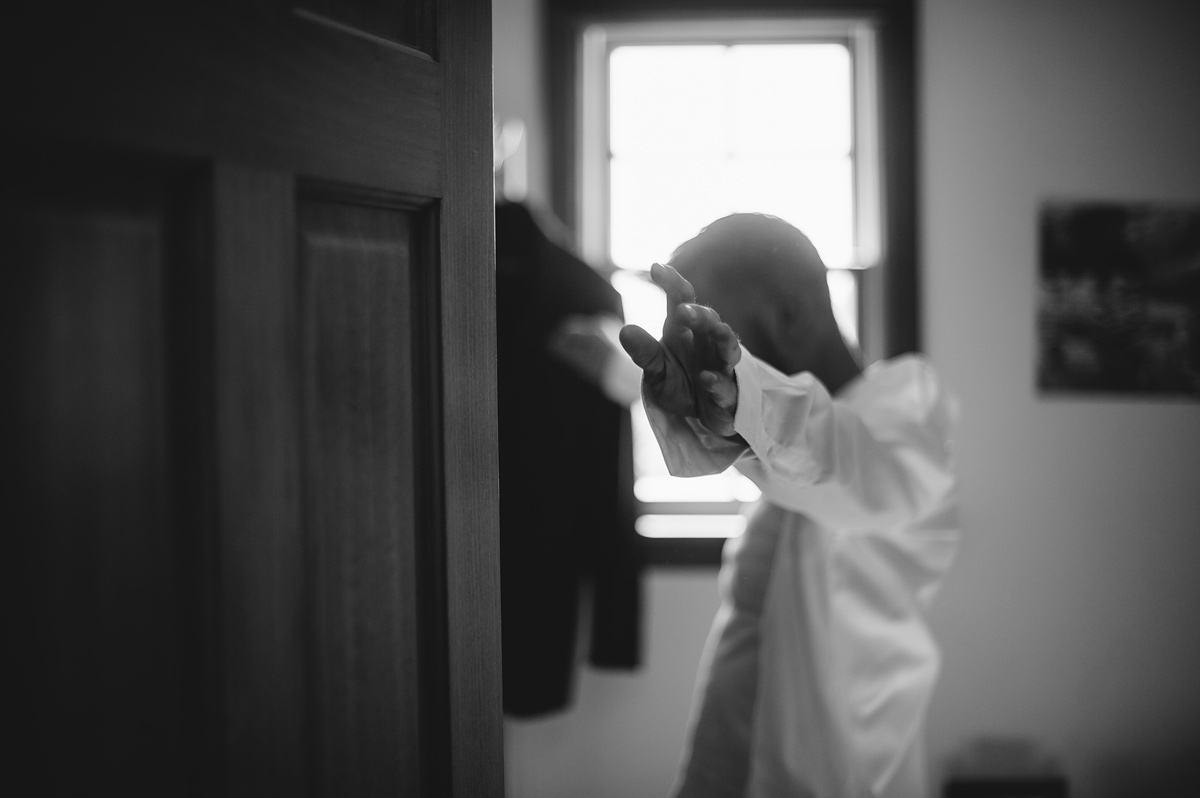 groom putting on shirt in black and white