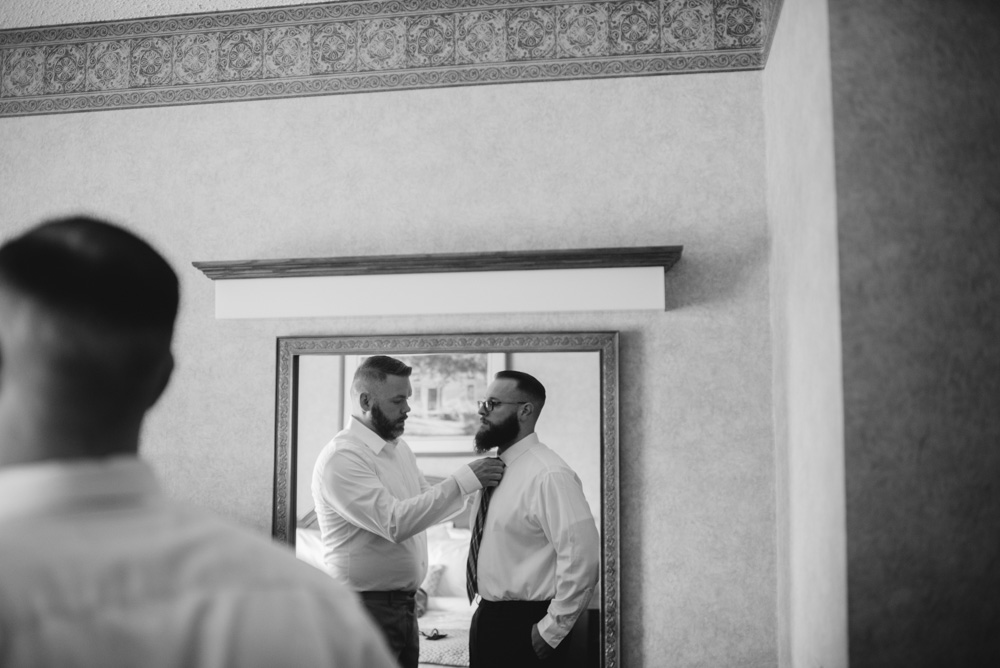 groomsman helps groom with tie