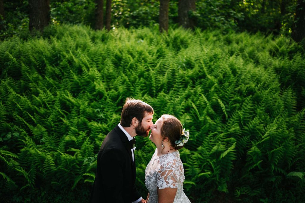 bride and groom kissing in front of ferns