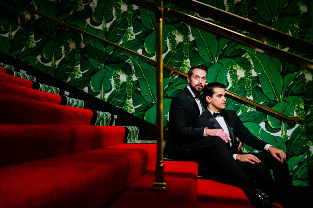 Gay couple sitting on red carpet stairs during their Greenbrier wedding.