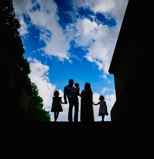 The silhouette of a family holding hands, with two children and parents standing against a bright sky filled with fluffy clouds.