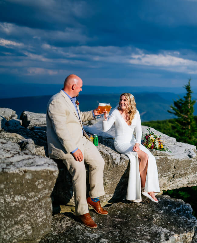 On top of a rugged mountain, a couple cheerfully toasts with beer.