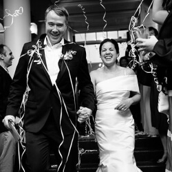 A newlywed couple walks through a shower of streamers, with the bride in a white gown and the groom in a classic tuxedo, surrounded by smiling guests.