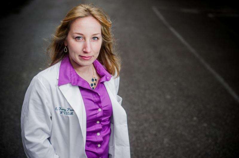 A woman stands outdoors with a doctor jacket.