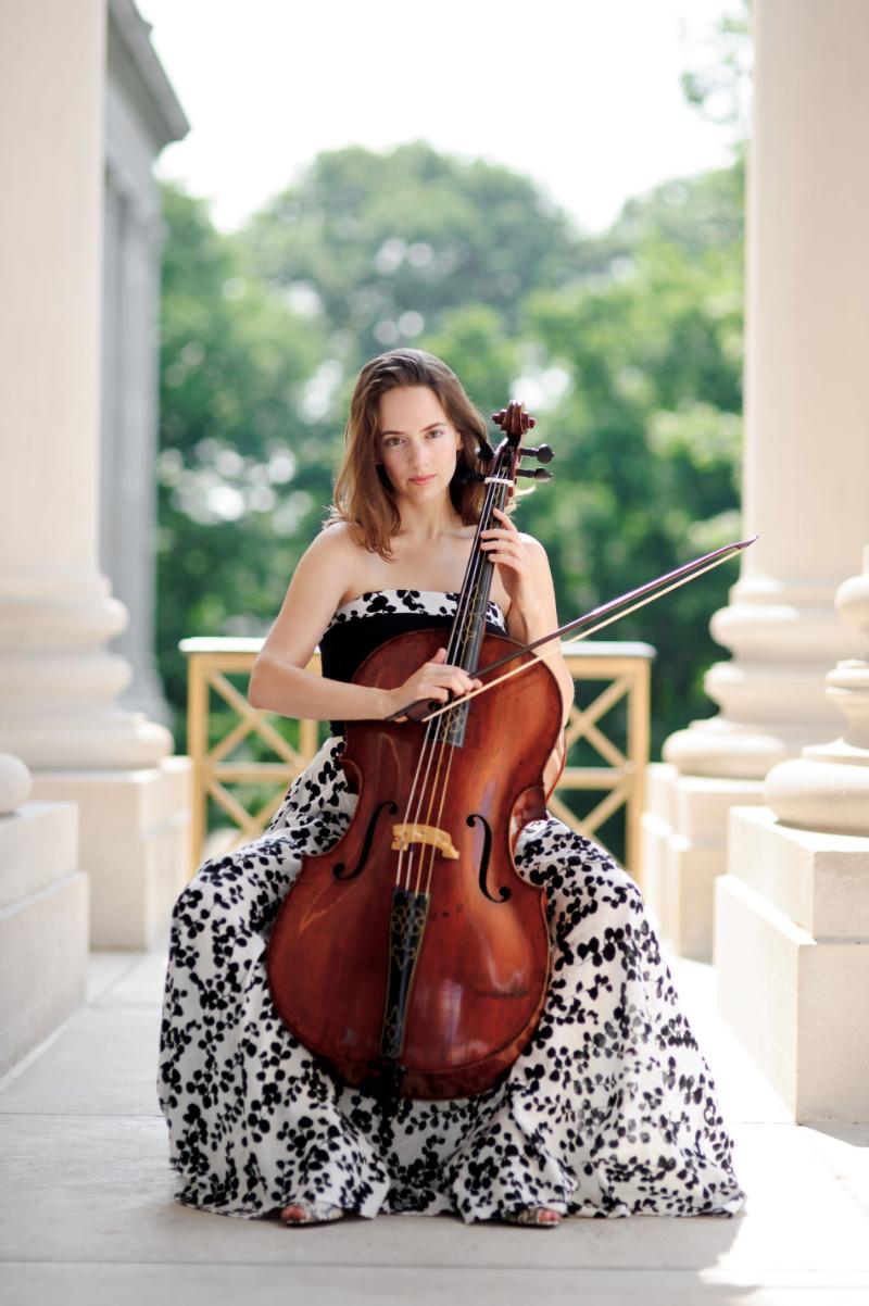 A woman in a dress plays the cello outdoors.