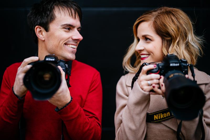 Two photographers smile looking at one another both holding cameras.