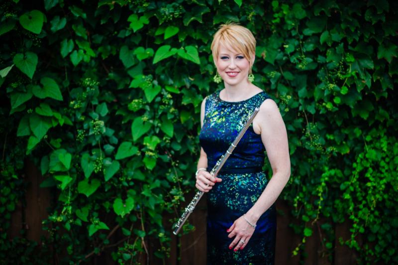 A woman holds her flute smiling in front of a green background.