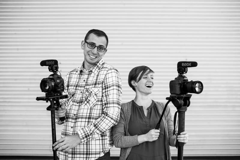 Two photographers hold their camera gear laughing.