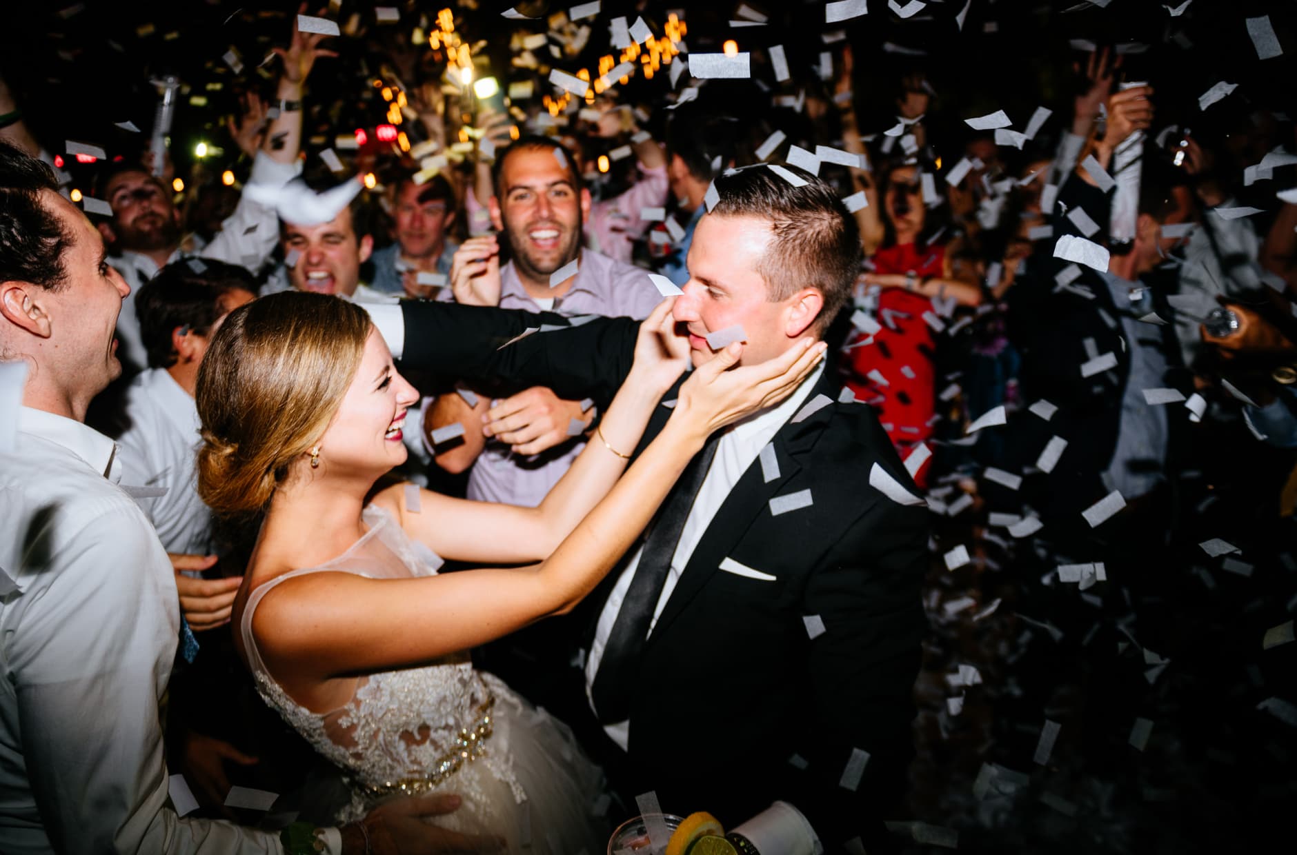 Amidst a lot of confetti, a bride touches the face of the groom, surrounded by family and friends.