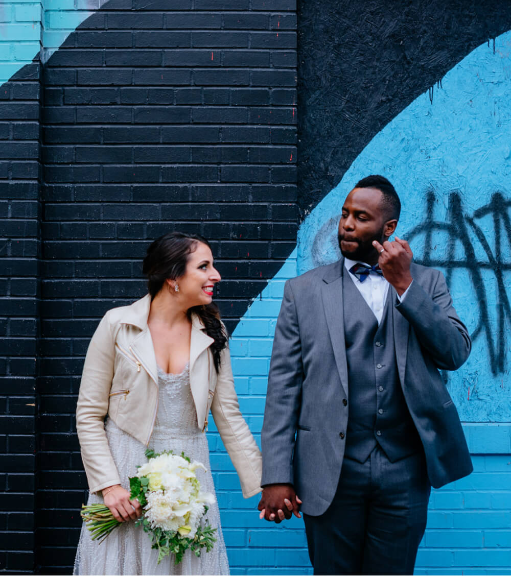 A stylish bride and groom stand against an urban backdrop of blue and black with graffiti art.