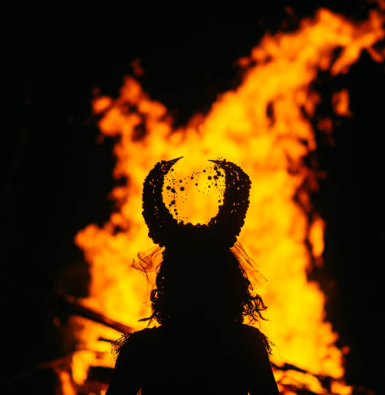 A striking silhouette of a bride, her veil adorned with details, stands in front of a vibrant, blazing fire in a dramatic way.