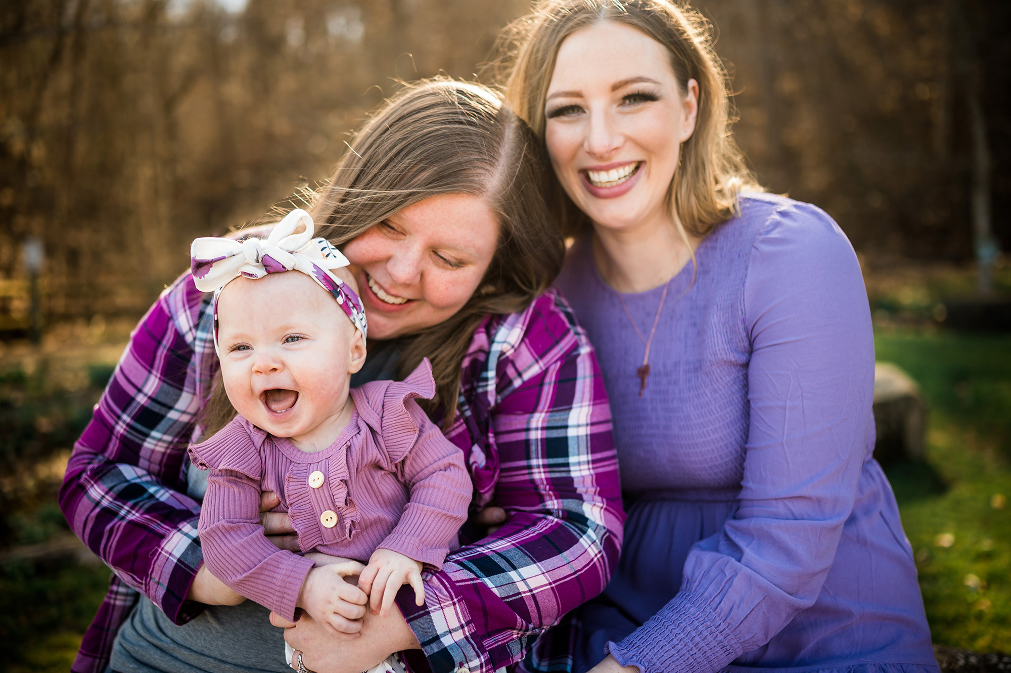 A happy family moment with two mothers, one holding a laughing baby wearing a bow.