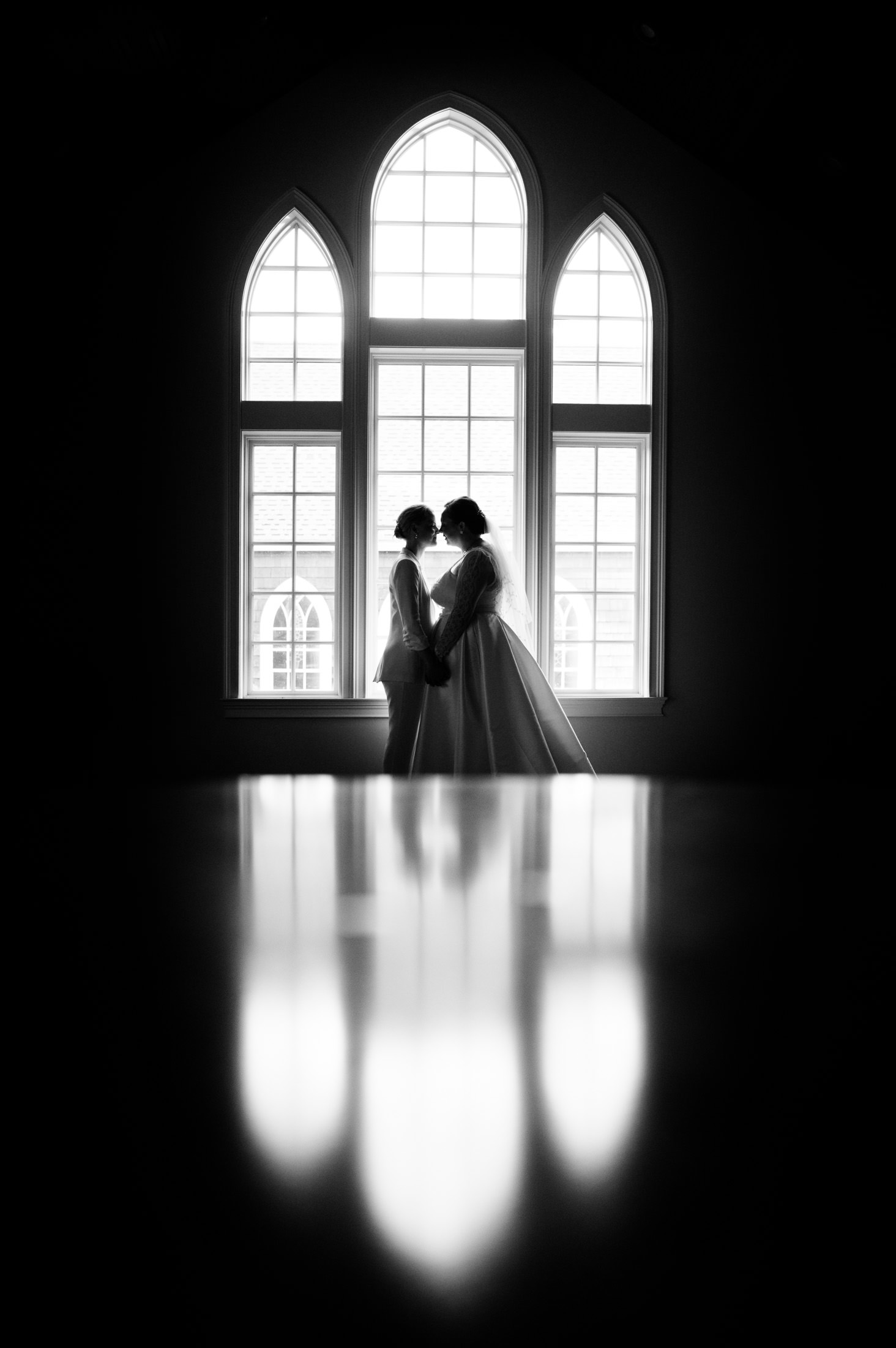 Silhouette of a couple standing close and facing each other, with large windows and a reflective floor creating a symmetrical aesthetic.