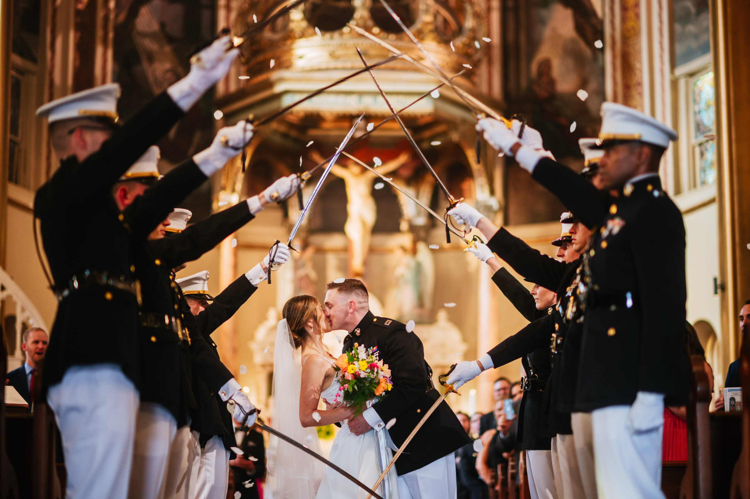 A bride and groom kiss under a traditional military arch at their wedding ceremony.