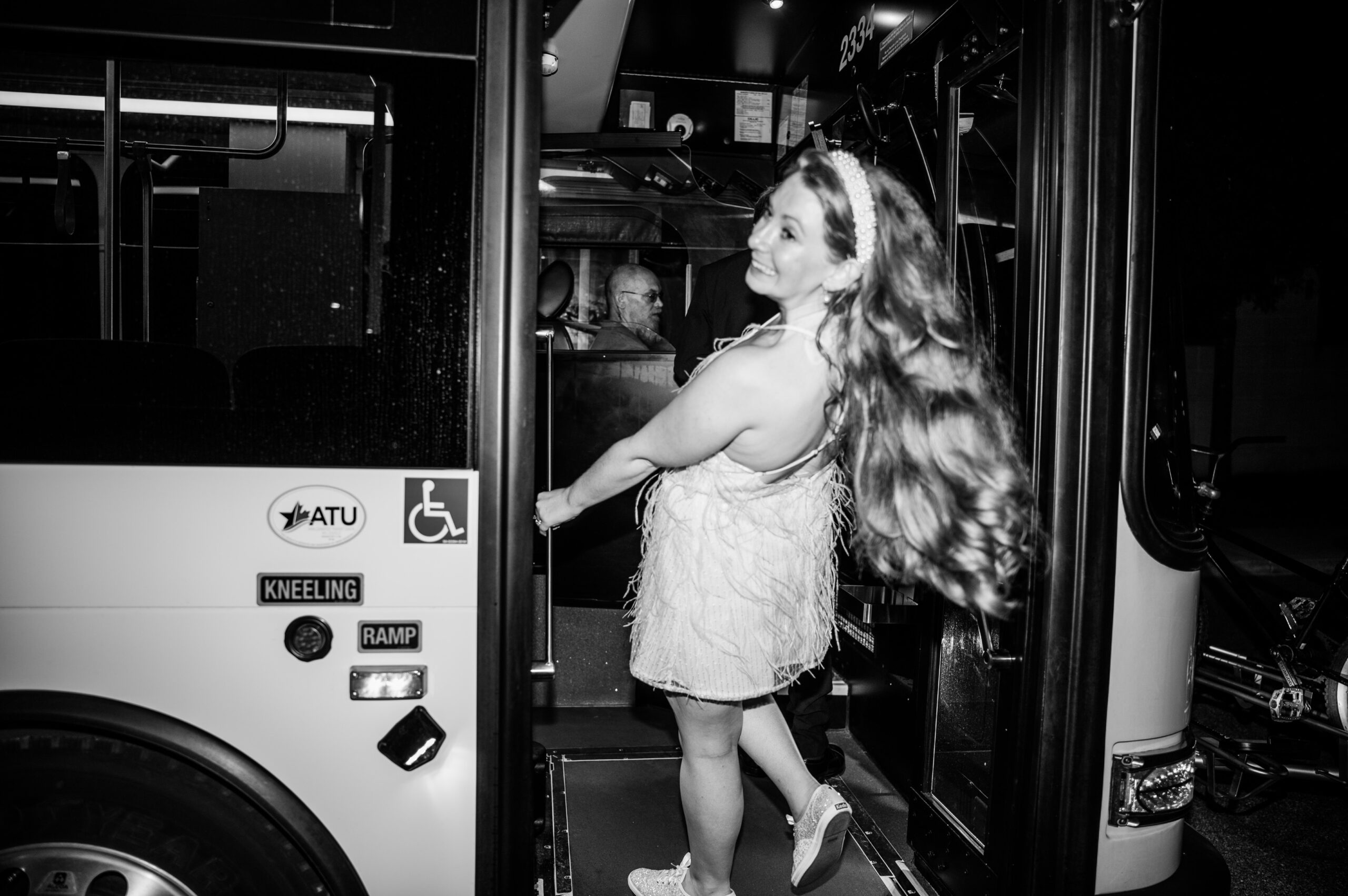 A woman in a sparkling white dress, happily stepping onto a bus.