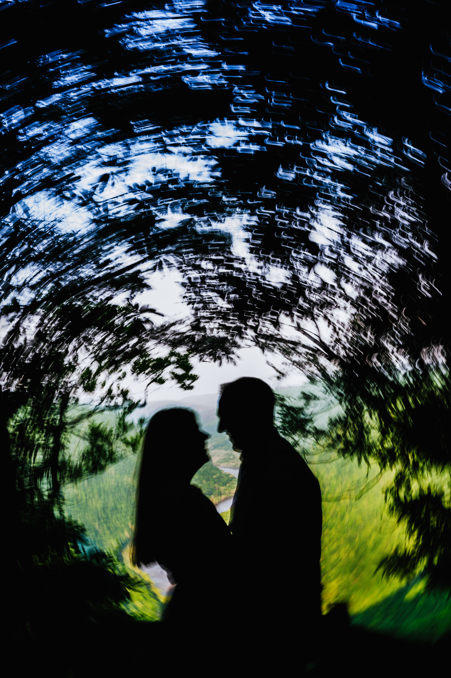 Silhouettes of a couple against a backdrop of trees and sky.