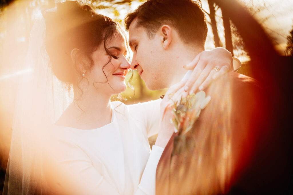 A close-up of a bride and groom about to kiss surrounded by warm sunlight.