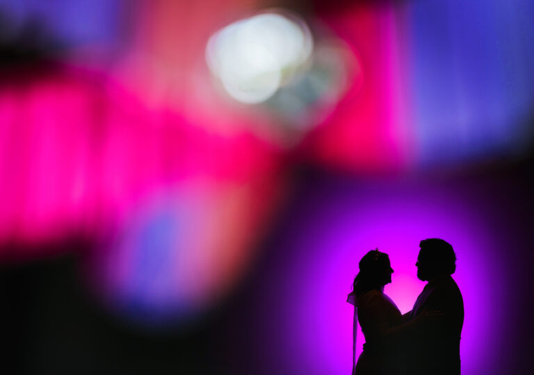 Kristin and Emmanuel embracing in silhouette, engulfed by a purple glow.