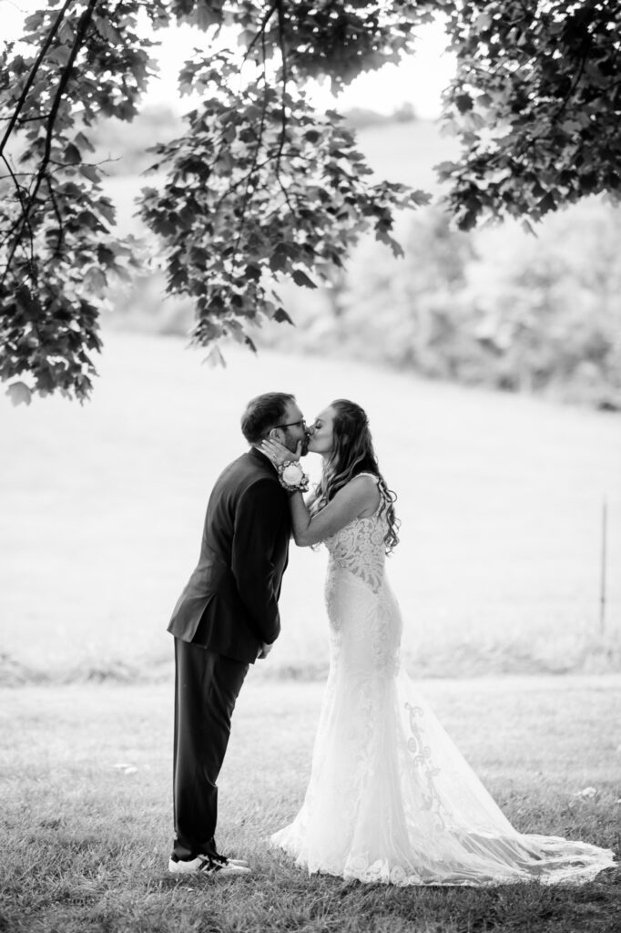 bride and groom kissing under tree during first look at batten green wedding venue