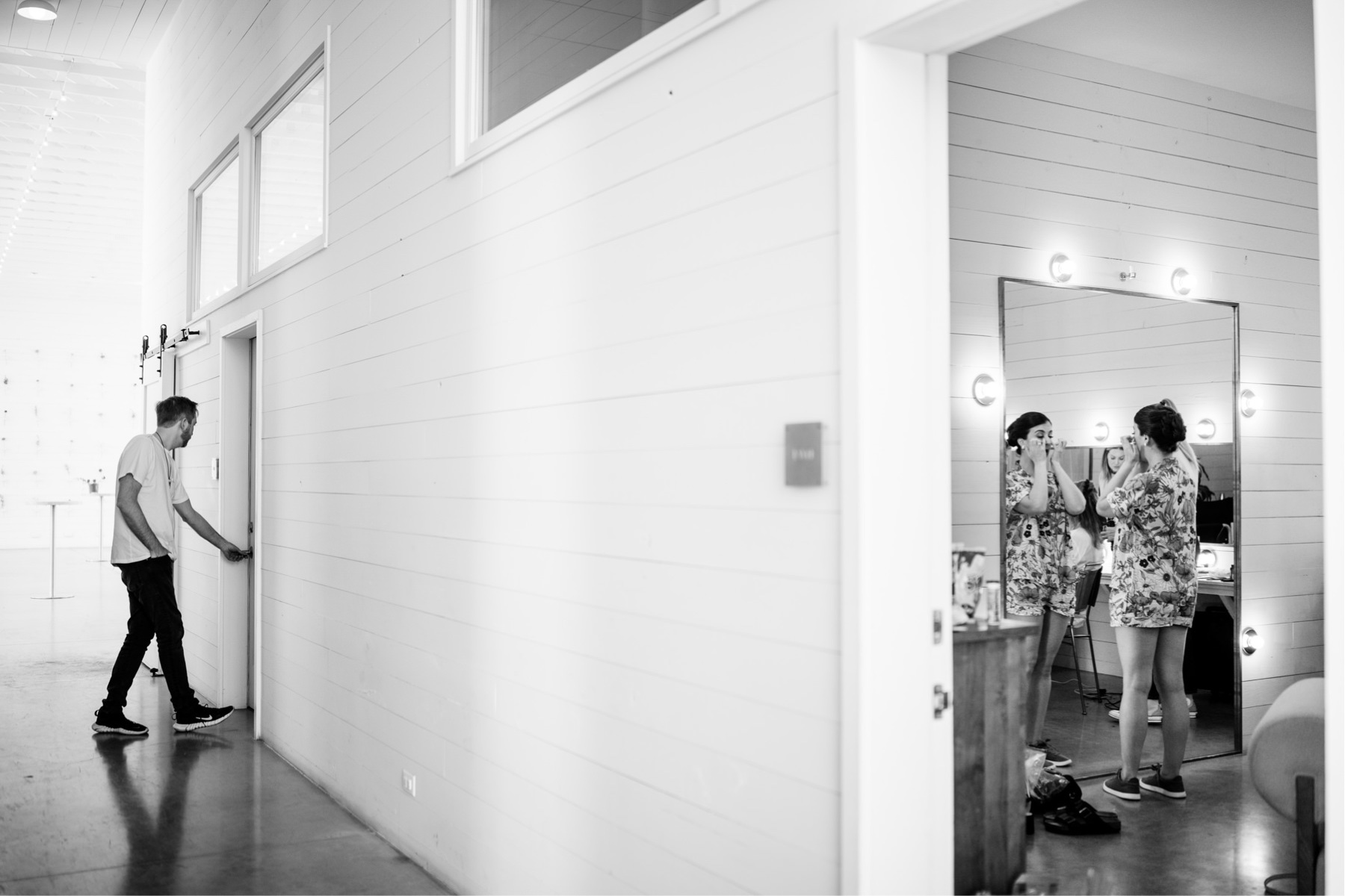 Groom entering doorway while bridesmaids apply makeup in a nearby room at Prospect House Austin TX wedding