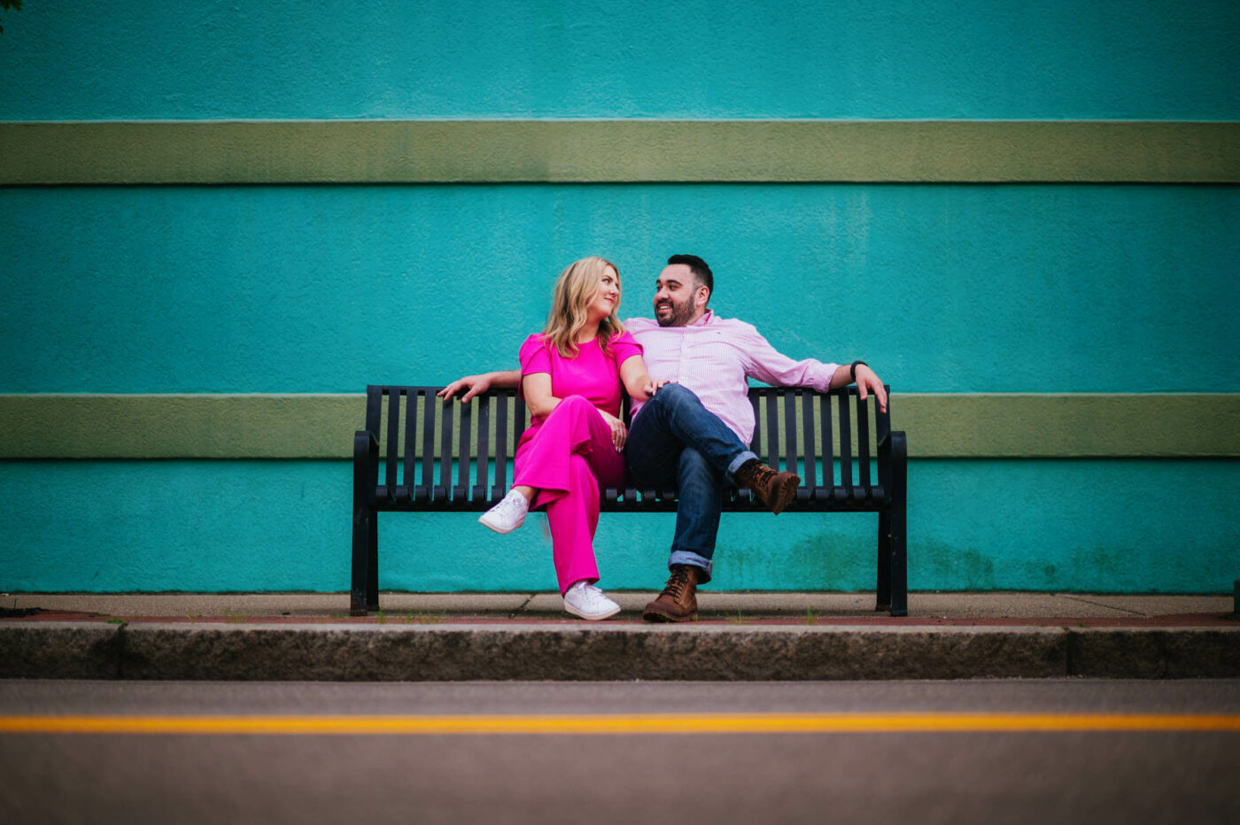 A couple enjoy a moment on a bench in front of a colorful wall during their engagement session in Charleston, WV.