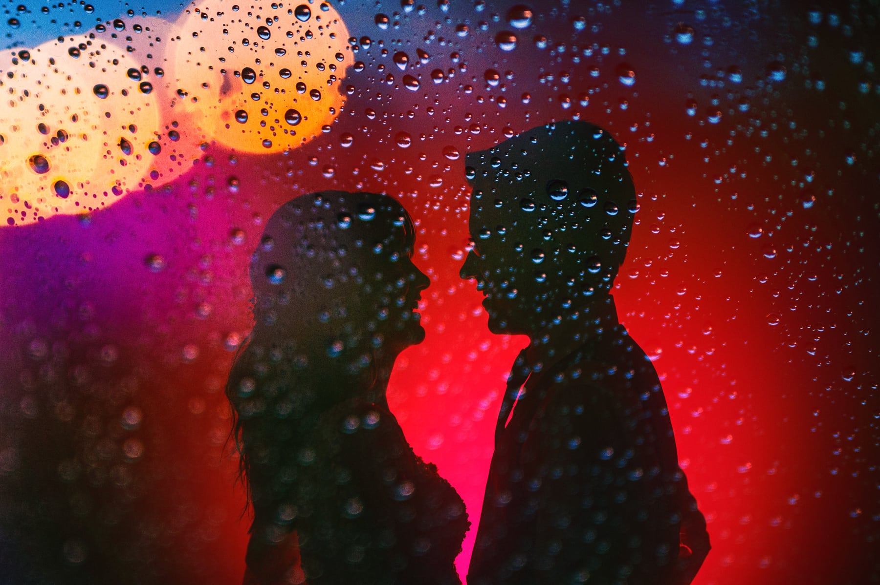 couple creative portrait silhouette with rain drops on glass and bright red 